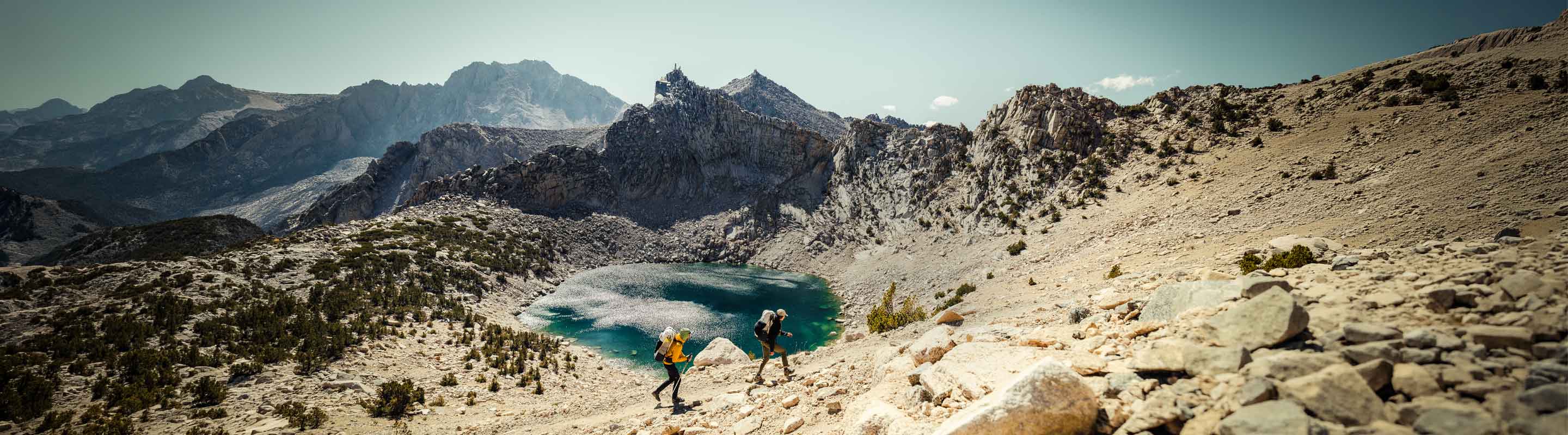 Two hikers near a mountain lake with a scenic mountain landscape.