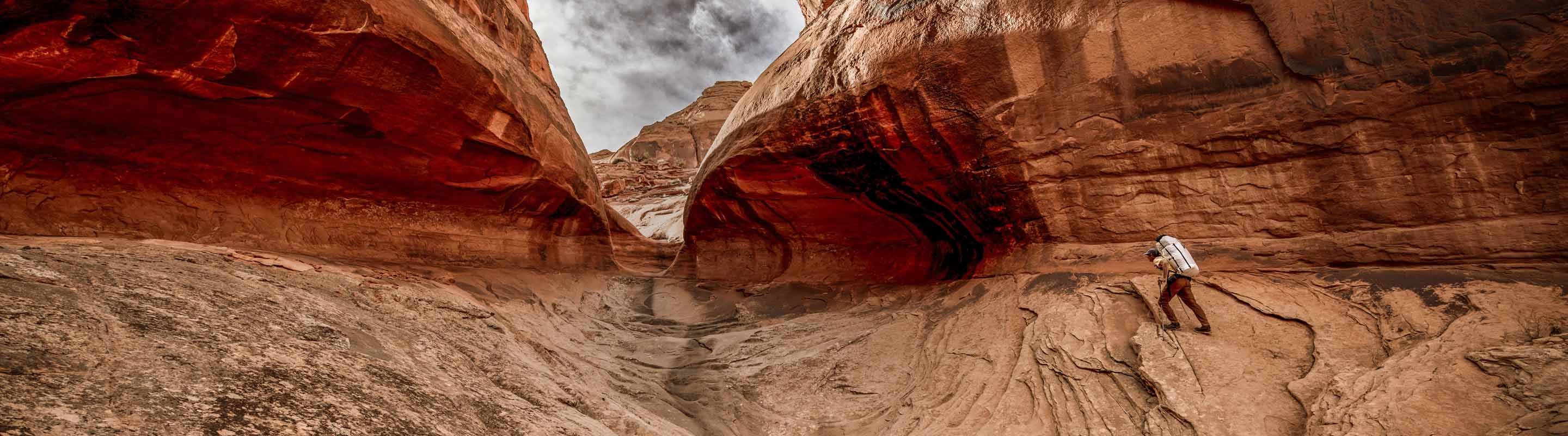 Person hiking through a desert canyon with red rock formations.