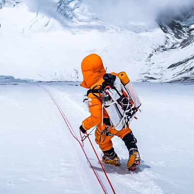 Person in orange winter gear climbing a snowy mountain