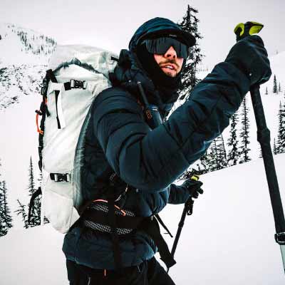 Person in winter gear with a backpack and ski poles in a snowy landscape