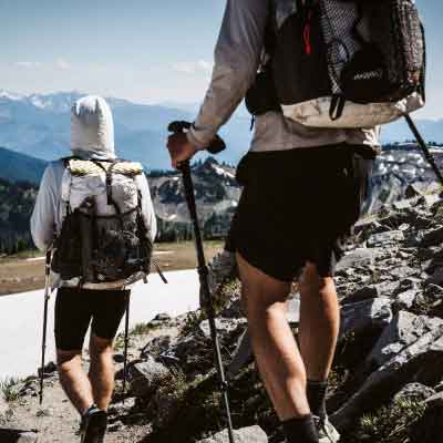 Two hikers with backpacks and walking sticks on a mountain trail.