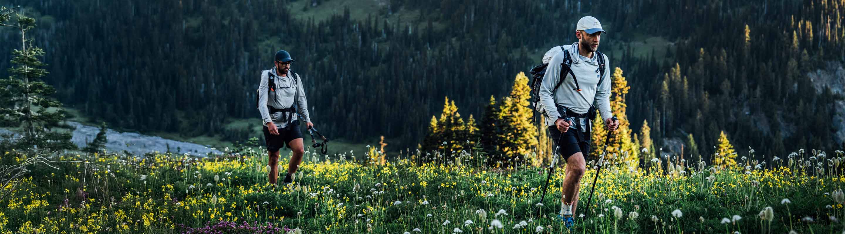 Two hikers in a mountainous area with greenery and a river in the background