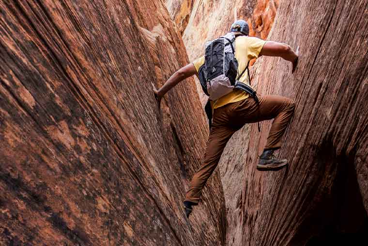 Person climbing a steep rock wall in a desert canyon