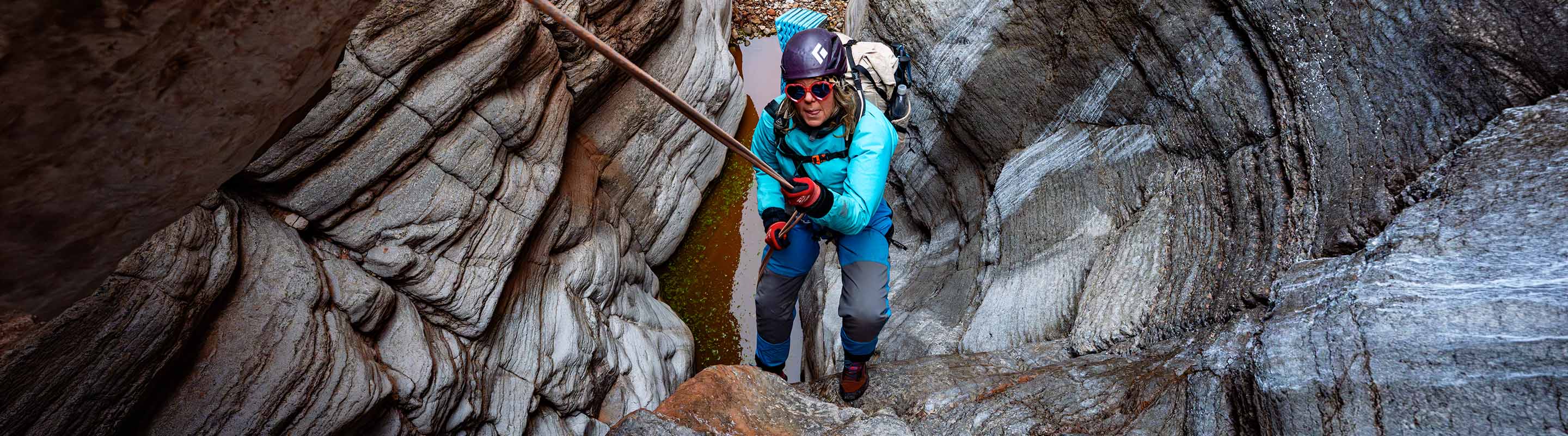 Person in a blue jacket and helmet scaling a cave with rocky walls 