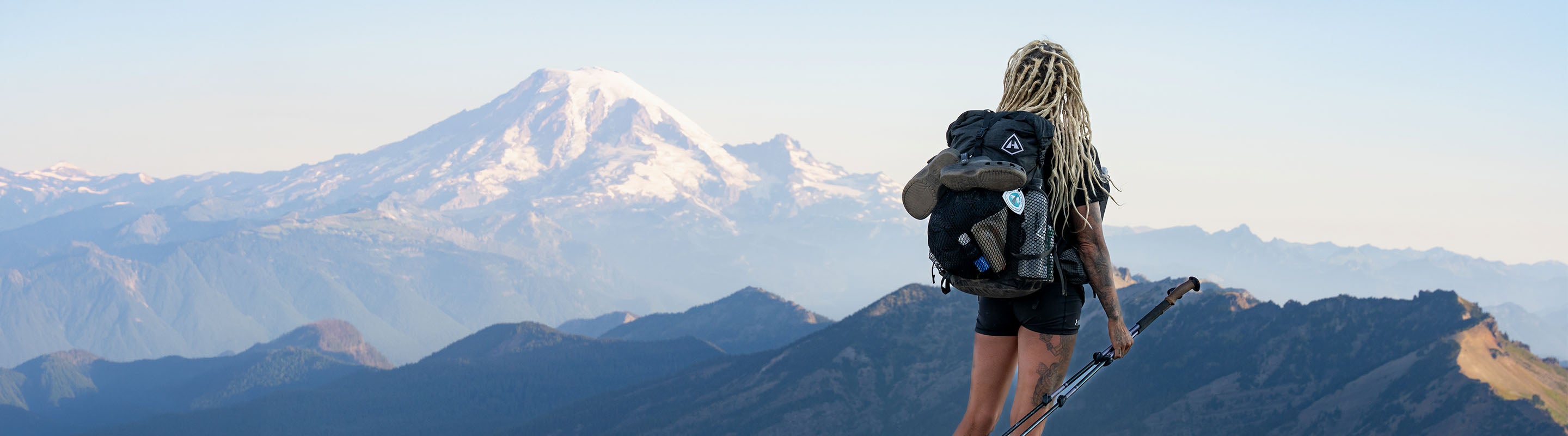 Person with a backpack standing on a mountain with snow-capped peaks in the background