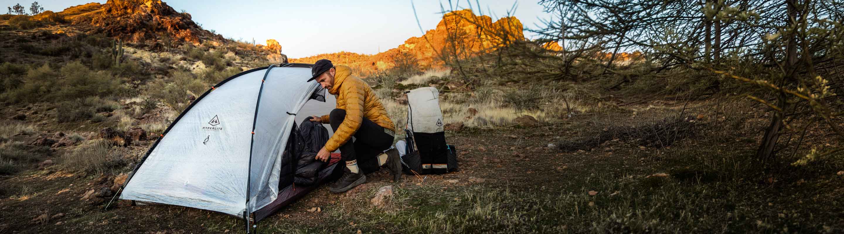Person setting up a tent in a natural outdoor setting with mountains in the background