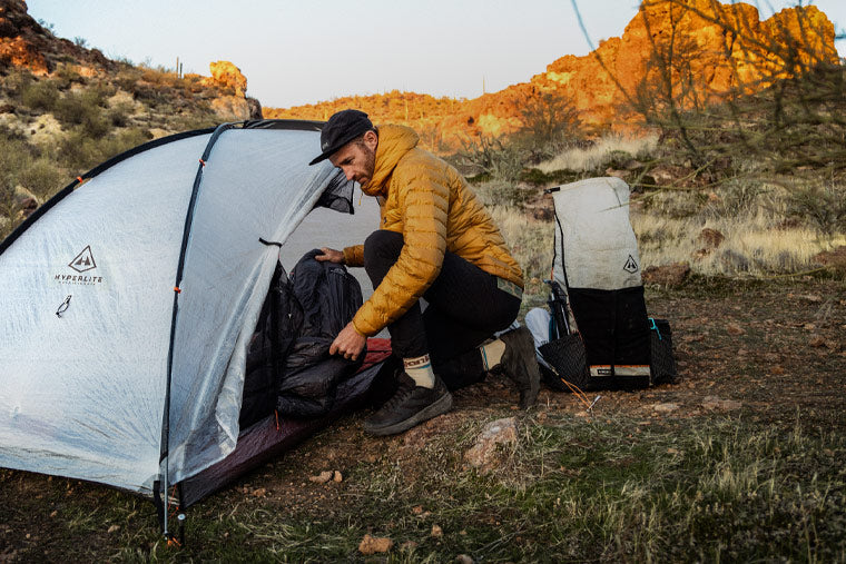 Person setting up a tent in a desert landscape with mountains in the background