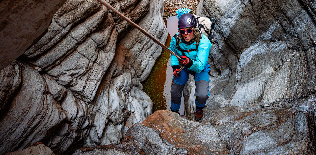 Person in a blue jacket and helmet navigating a rocky, narrow passage.