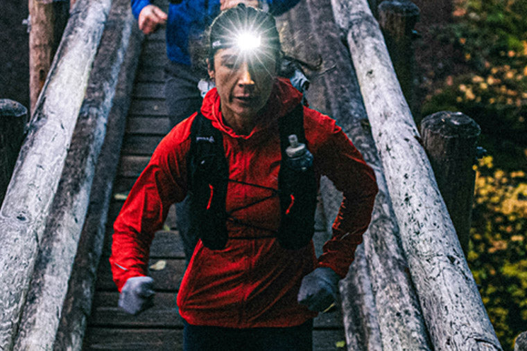 Person in red jacket running up a wooden staircase with a headlamp on.